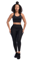 Front full view of a woman with a black sports bra and black leggings with her hands in both side pockets