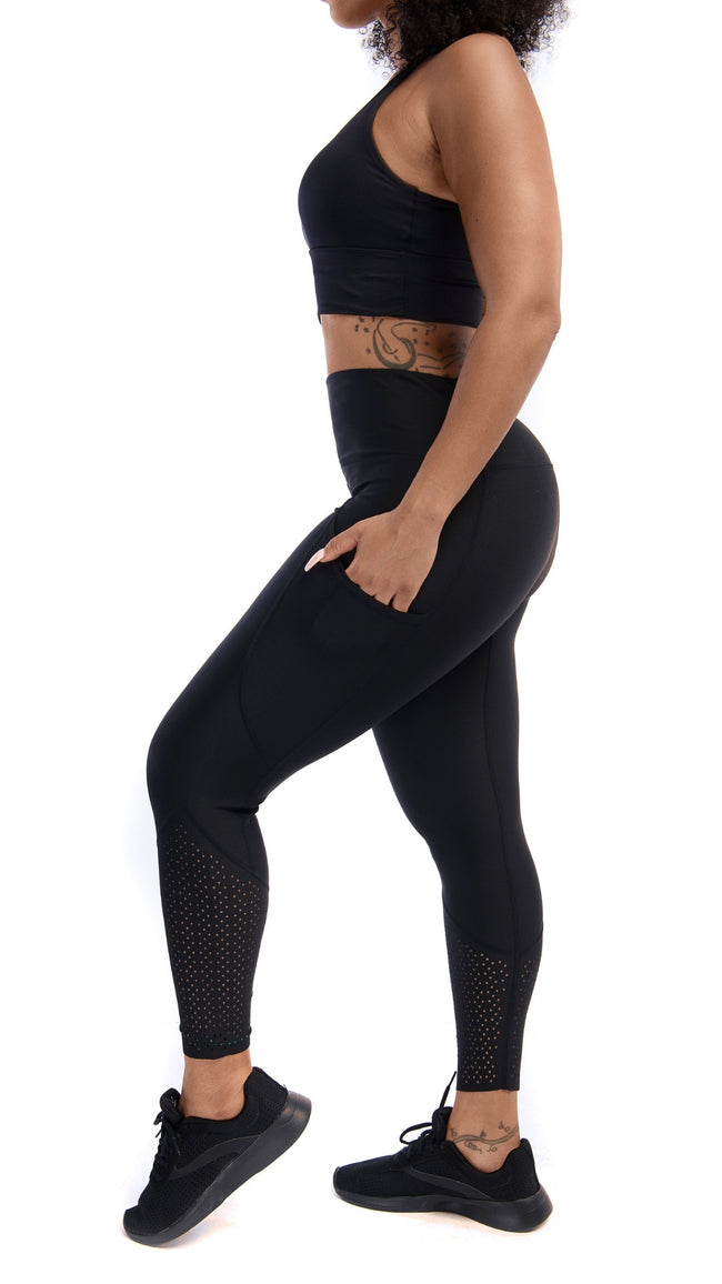 Side full view of a woman with a black sports bra and black leggings with her hand in side pocket